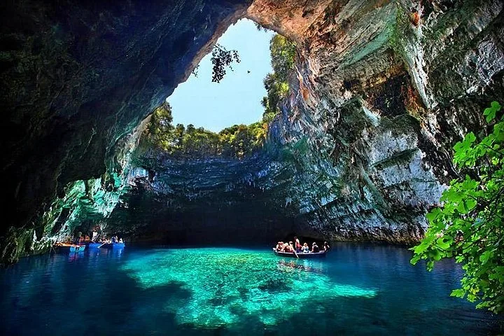Tourists on small boats enjoying the vibrant blue Melissani Cave lake.